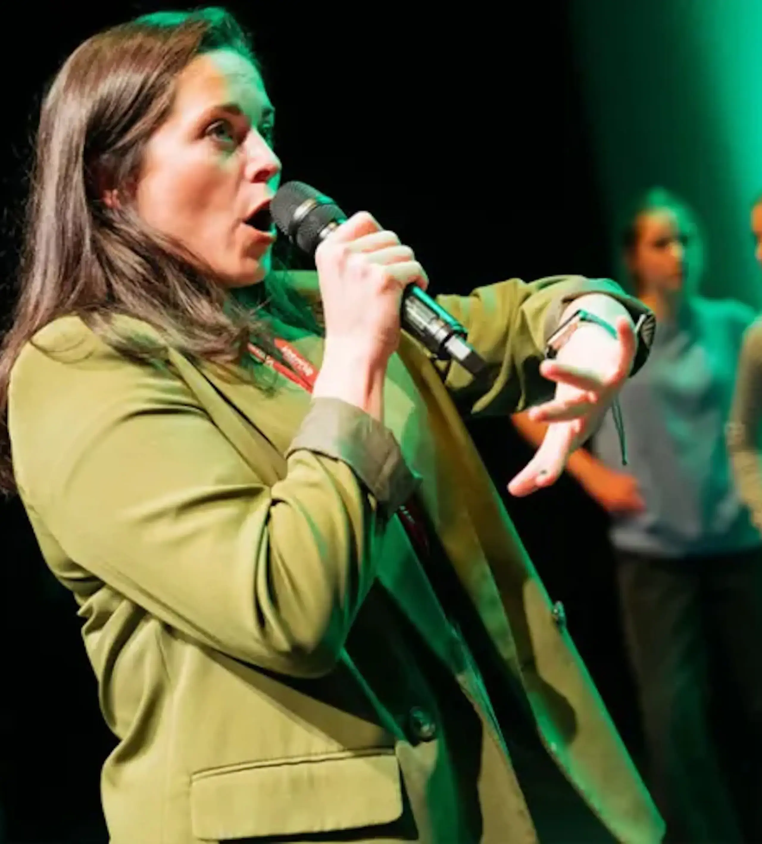 Guest in green blazer speaks or sings into microphone